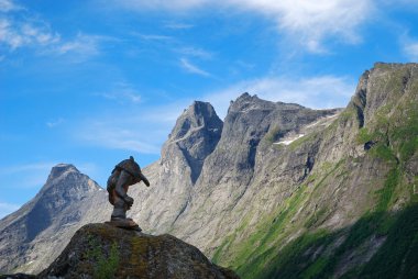 Wooden troll against mountain crest and blue sky. Trollstigen. clipart