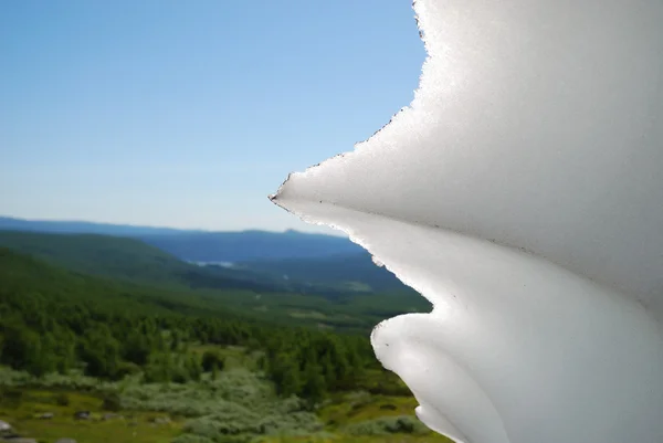 Melting snowfield against the summer green hills. — Stock Photo, Image