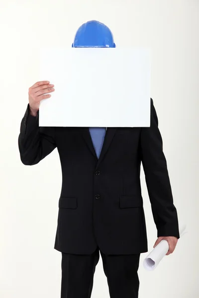 Empresario de la construcción escondiendo su cara con un cartel en blanco —  Fotos de Stock