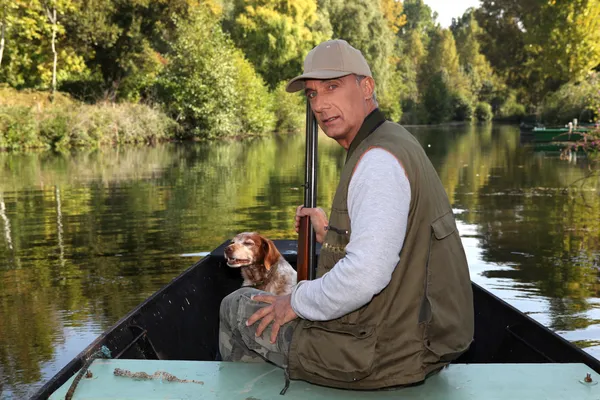 Caçador com uma caçadeira e cão em um barco — Fotografia de Stock