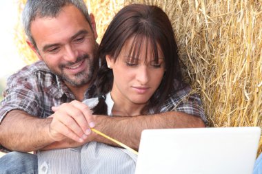 Farming couple sat with laptop computer clipart