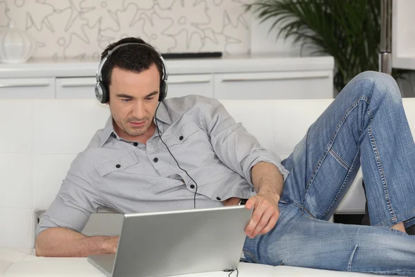 Man liggen op een bank met zijn laptop en een paar hoofdtelefoons — Stockfoto