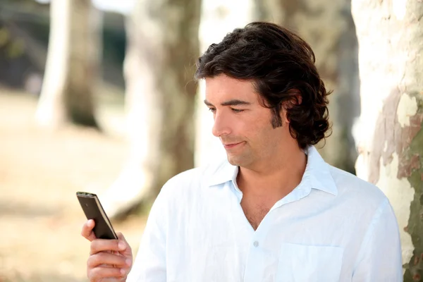 Un uomo nel parco che legge un messaggio sul suo cellulare — Foto Stock