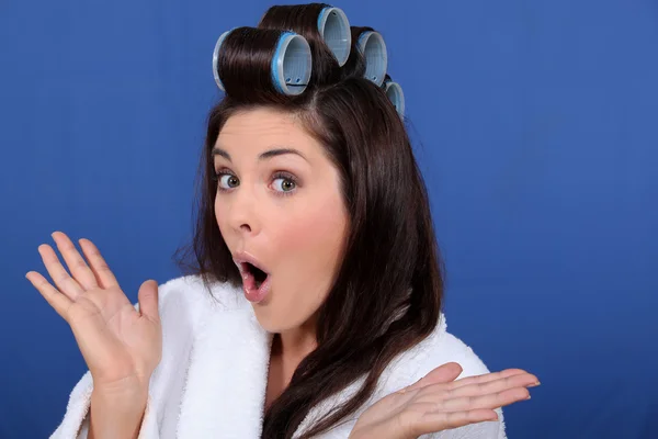 Morena bonito em roupão de banho com encrespadores de cabelo contra fundo azul — Fotografia de Stock