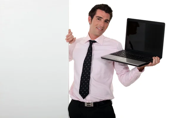Negocio sosteniendo un ordenador portátil y de pie junto a un signo en blanco — Foto de Stock