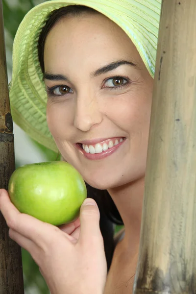 Γυναίκα που είναι χαμογελώντας με πράσινο καπέλο και μήλο — Φωτογραφία Αρχείου