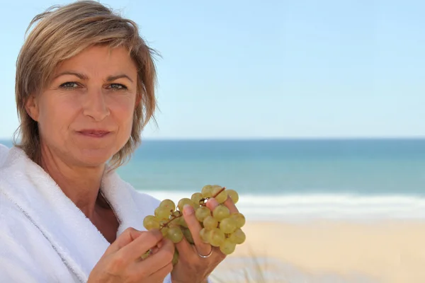 Midden leeftijd vrouw druiven eten in de buurt van de zee — Stockfoto