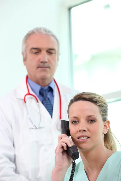 Медсестра разговаривает по телефону, пока доктор стоит в стороне — стоковое фото