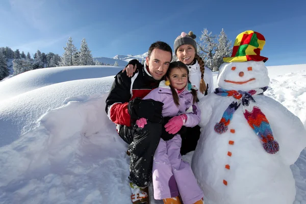 Couple posing with child beside snowman at mountain resort — Stock Photo, Image
