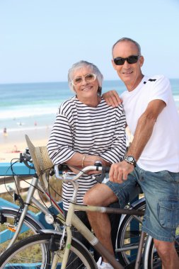 Senior couple riding bikes on the beach clipart