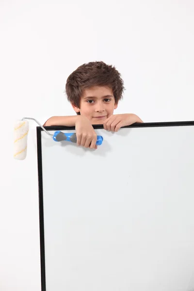 Young boy with a paint roller and a large board left blank for your message — Stock Photo, Image