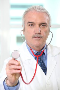 Doctor holding up the chestpiece of his stethoscope clipart