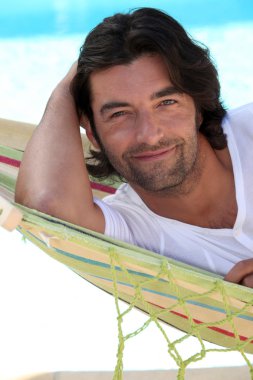 Man at beach laid in hammock clipart