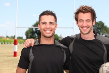 Two rugby players posing with ball in front of goal clipart