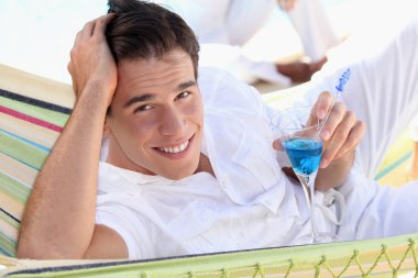 Young man enjoying a cocktail in a hammock clipart