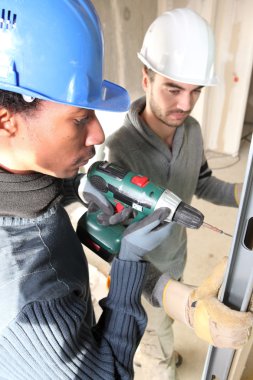 Black and white carpenters at work with electric drill clipart