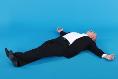 Mature man in suit lying on his back with arms wide apart against blue back clipart