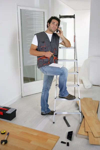 寄木細工の床を置くと、携帯電話で話している職人 — ストック写真