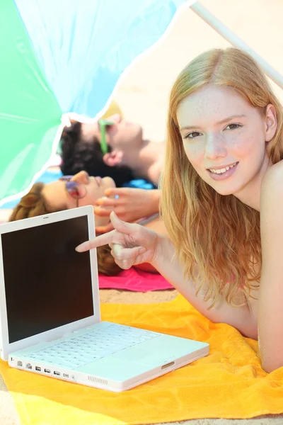 Menina bonita apontando seu laptop enquanto seus amigos estão bronzeando — Fotografia de Stock