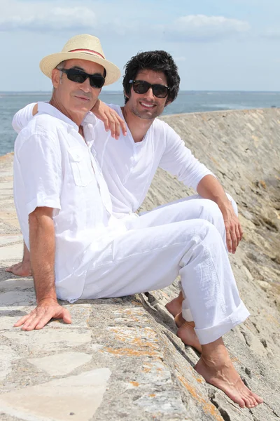Взрослые отец и сын сидят на стене гавани — стоковое фото