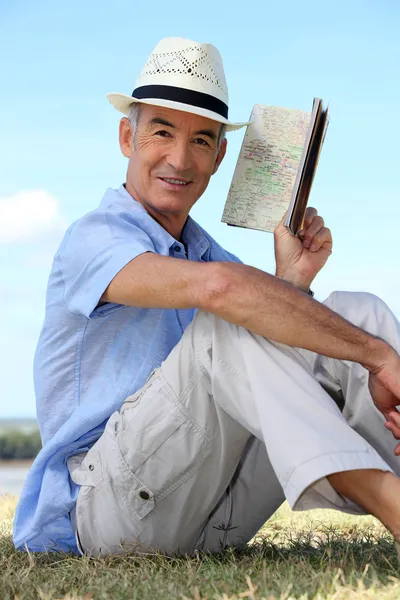 Старик, сидящий на траве и читающий старый блокнот — стоковое фото