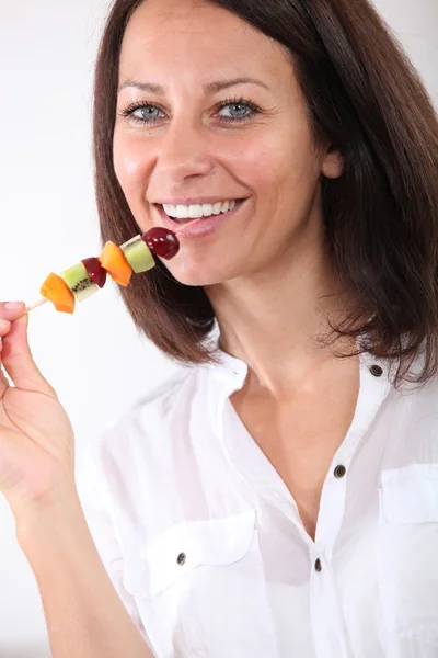 Femme de 40 ans mangeant une brochette de fruits — Photo