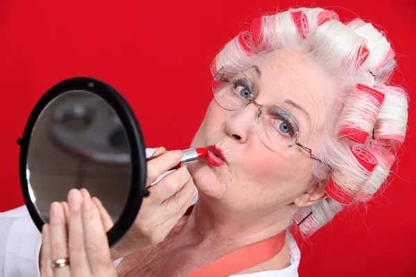 Senior vrouw met krulspelden in het haar zetten lippenstift — Stockfoto