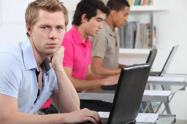Tres estudiantes varones con ordenadores portátiles en el aula —  Fotos de Stock