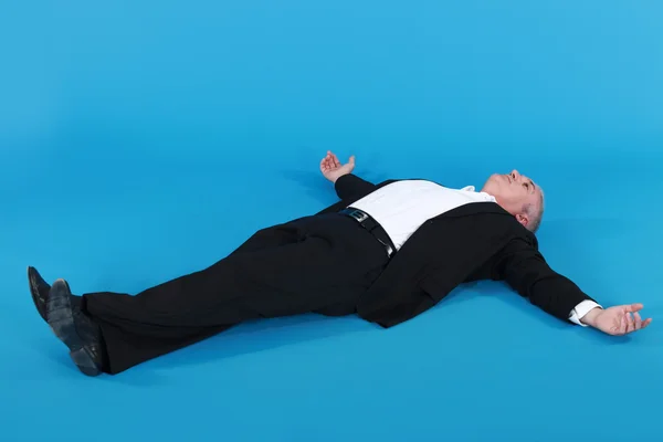 Uomo maturo in tuta sdraiato sulla schiena con le braccia divaricate contro la schiena blu — Foto Stock