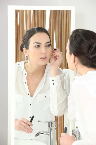 Junge Frau trägt Mascara vor einem Badezimmerspiegel auf — Stockfoto