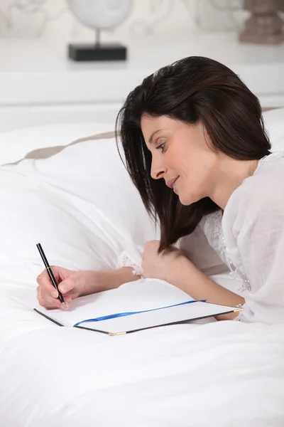 Жінка лежала на своєму ліжку, пишучи на блокноті — стокове фото
