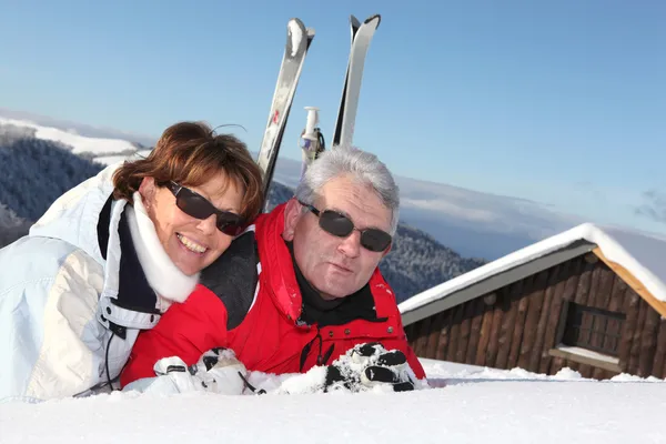 Äldre par liggande i snön utanför deras ski stuga — Stockfoto