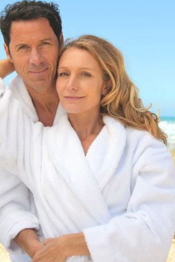 Man and woman in toweling robes on the beach clipart