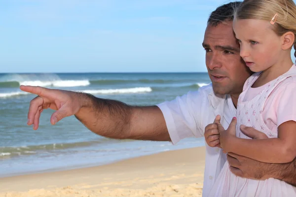 Батько і дочка вказують на щось на пляжі — стокове фото