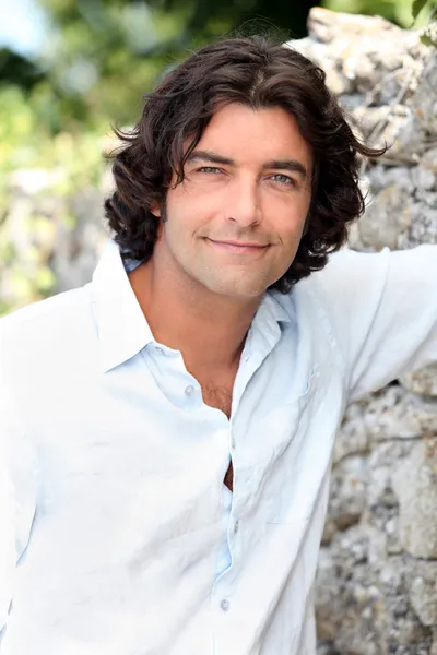 Handsome man with long hair standing by an old stone wall — Stock Photo, Image