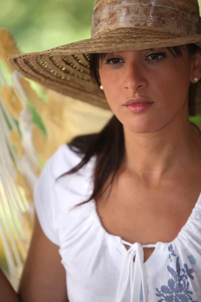 Созерцательная женщина в соломенной шляпе сидит в гамаке — стоковое фото