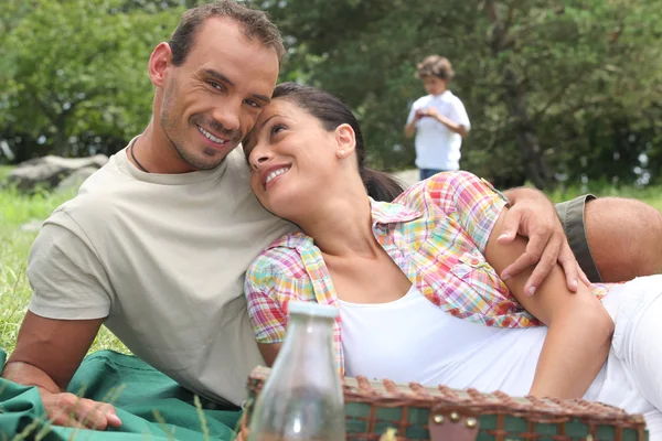 Giovane coppia avendo un picnic con bambino in background — Foto Stock