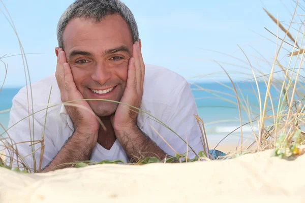 Homem feliz deitado na areia — Fotografia de Stock