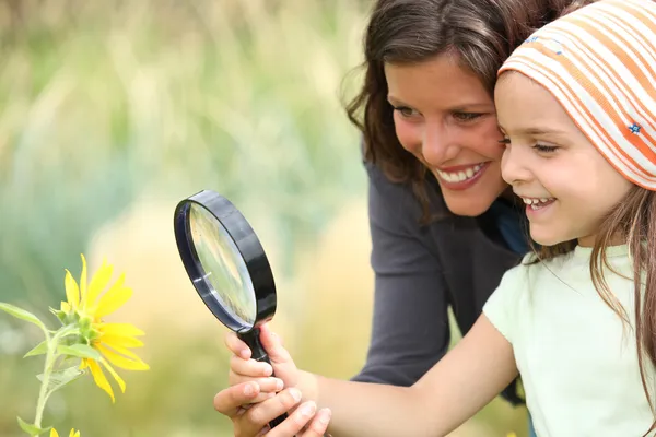 母亲和女儿检查使用放大镜一朵花 — 图库照片