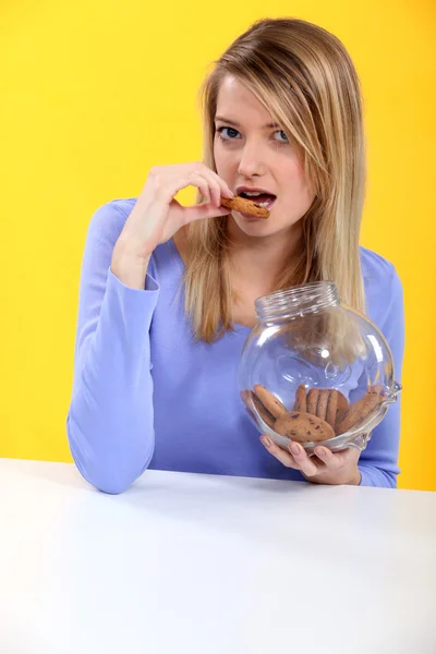 Cantik pirang makan cookie terhadap latar belakang kuning — Stok Foto