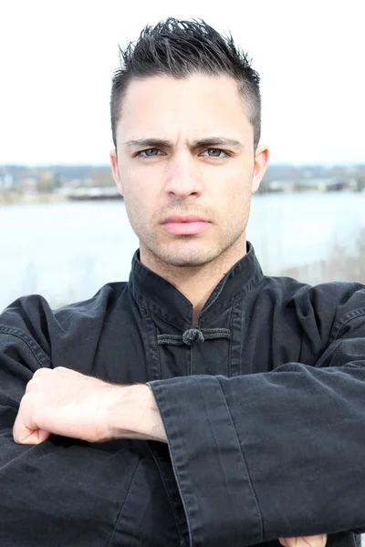 Uomo vestito con una giacca nera di arti marziali in piedi vicino a un fiume — Foto Stock