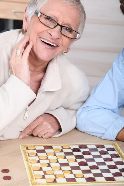An old laughing lady playing checkers with somebody. — Stock Photo, Image