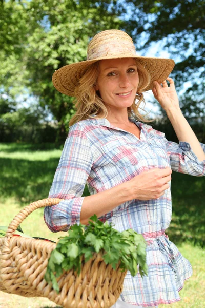 Mujer sosteniendo sombrero de paja y cesta de verduras . — Foto de Stock