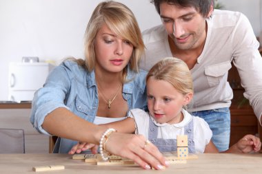 A cute little girl playing dominos with her parents. clipart