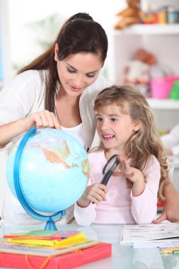 Mother and daughter looking at a globe with a magnifying glass clipart