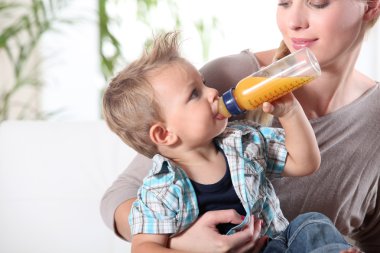 Child drinking juice in his mother's lap clipart