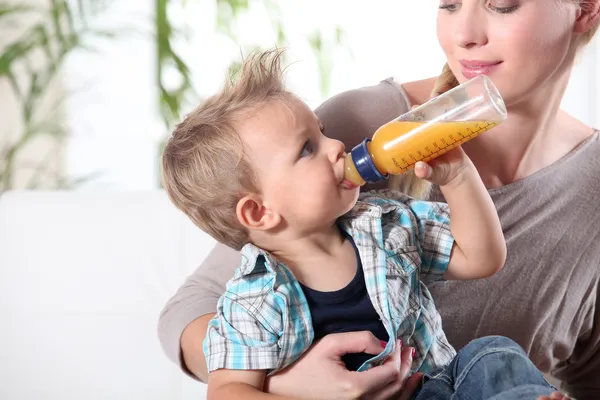 Ребенок пьет сок на коленях матери — стоковое фото