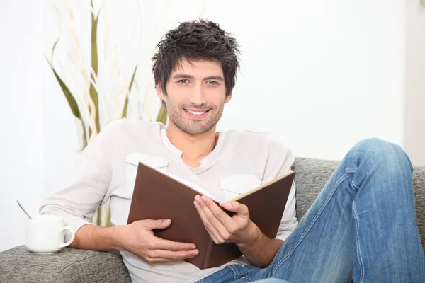 读一本书在沙发上的男人 — 图库照片