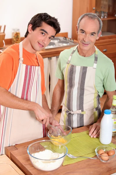 Een jonge man en zijn grootvader dragen schorten en het maken van een taart — Stockfoto