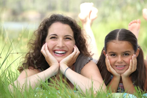A woman and a little girl lying down in the grass — Stock Photo, Image